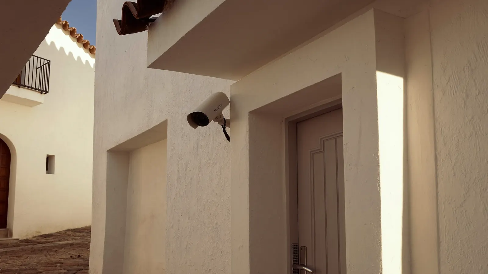 Cámara de seguridad bajo el alero de una casa encalada de Sevilla, enfocando su propia puerta